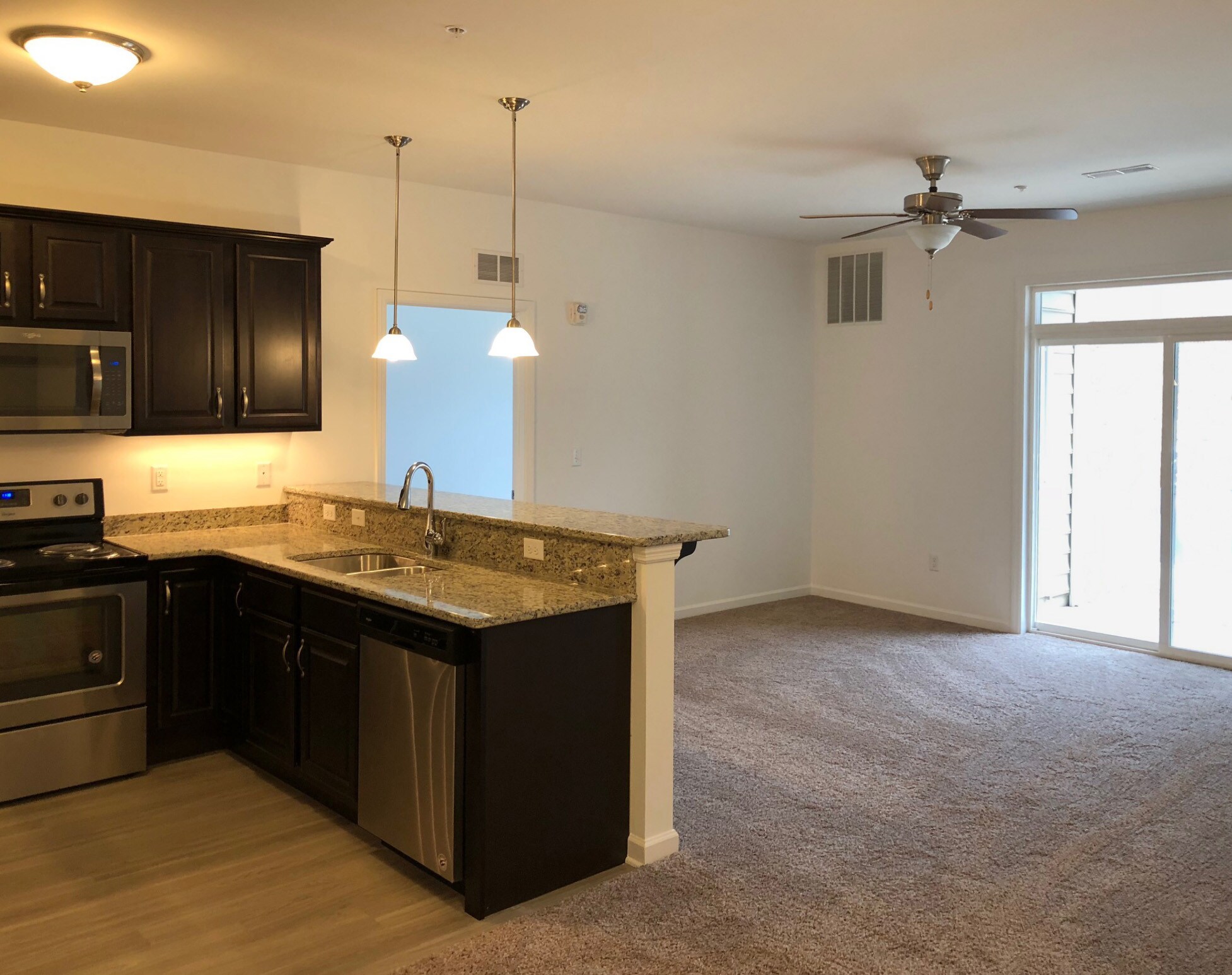 Kitchen with granite breakfast bar and pendant lights beside a carpeted living room with ceiling fan