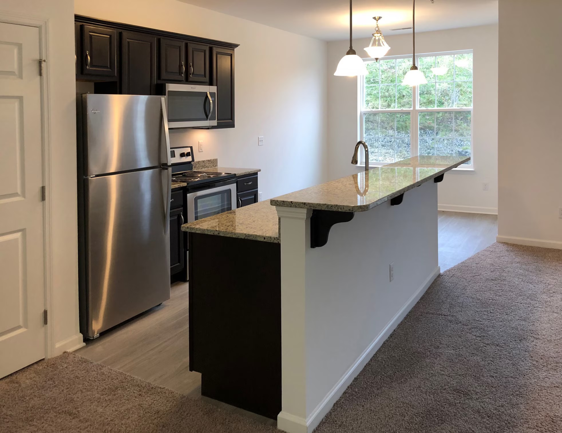 Kitchen island with granite counter and pendant lights in front of a bright window